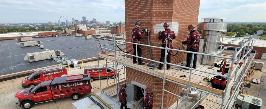 Mad Hatter technicians in safety harnesses working on a commercial brick chimney from rooftop scaffolding in St. Louis